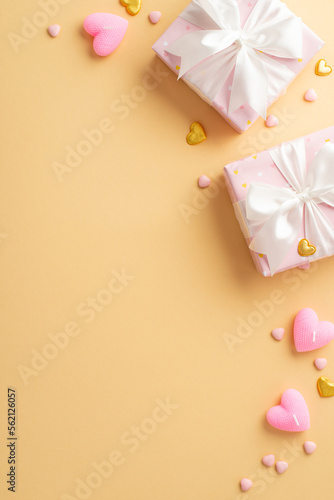 Valentine's Day concept. Top view vertical photo of pink present boxes with white ribbon bows golden hearts candles and sprinkles on isolated pastel beige background with copyspace © ActionGP