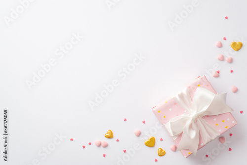 Valentine s Day concept. Top view photo of pastel pink present box with silk ribbon bow golden hearts and sprinkles on isolated white background with copyspace