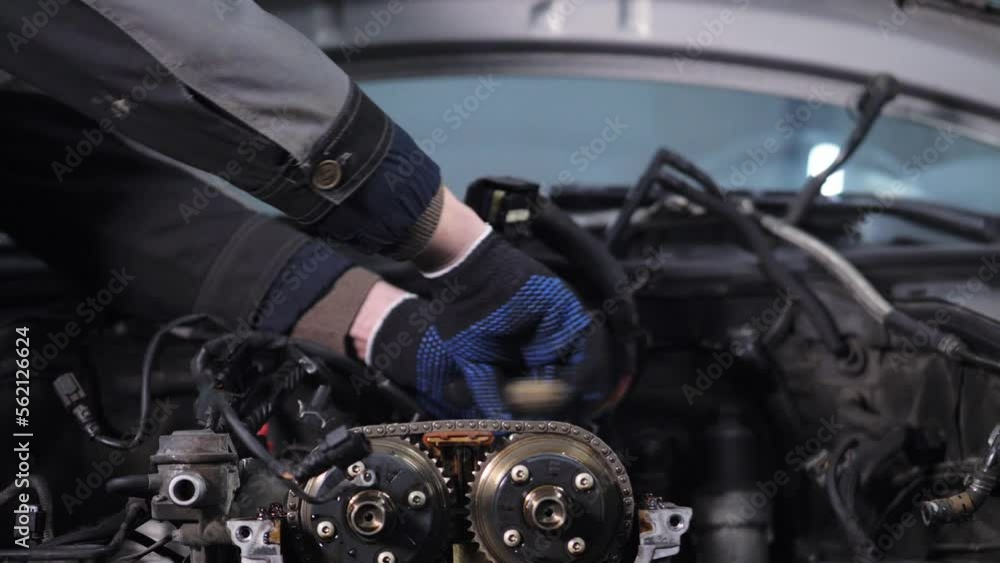 Hands of a mechanic in gloves unscrew the camshaft bolt in the engine. A male mechanic repairs a car in a car service. Car repair Hands of a mechanic in gloves unscrew the camshaft bolt in the engine. A male mechanic repairs a car in a car service. Car repair