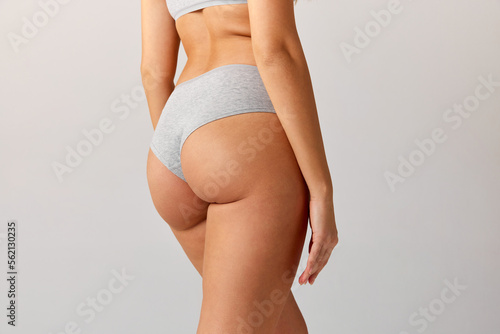 Cropped image of slim, fit female body, buttocks in cotton underwear over grey studio background. Anti-cellulite care. Concept of body and skin care, fitness