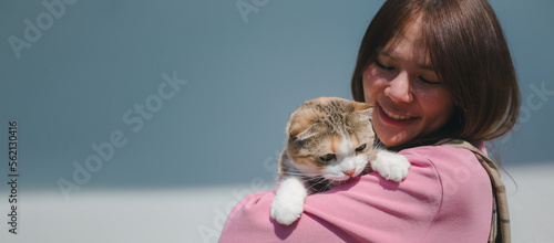 Young attractive Asian woman holding a cat with smiley face standing outdoor in the morning light sun beam. Pets makes people happy and relief the stress. Lovely kitty with girl.