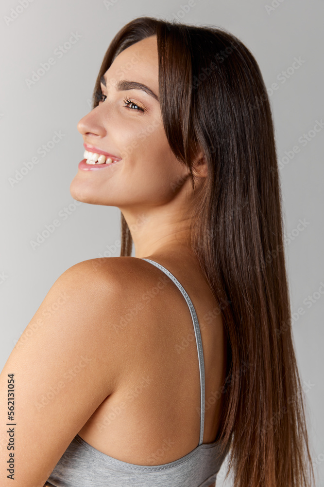 Portrait of young beautiful girl with straight brunette hair posing over grey studio background. Cosmetology care. Concept of body and skin care, fitness Portrait of young beautiful girl with straight brunette hair posing over grey studio background. Cosmetology care. Concept of body and skin care, fitness