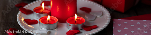 Saint Valentine's Day celebration. Red burning candles, hearts, gift box, postcard on dark wooden background. Happy holiday. Table decor for festive dinner, romantic atmosphere. Banner photo