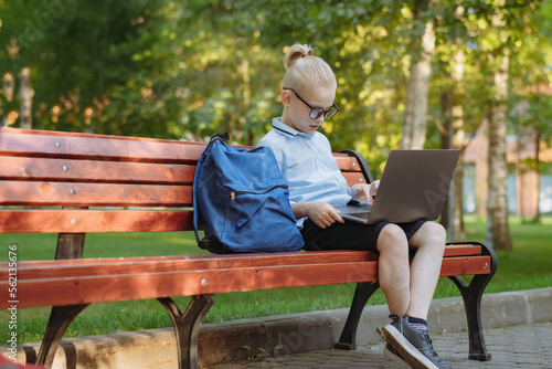 cute caucasian boy sitting on bench in park with laptop computer. Black screen