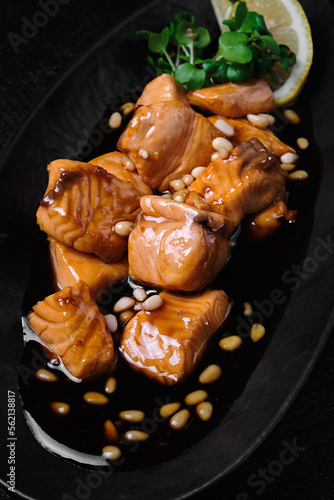 salmon in teriyaki sauce with pine nuts and lemon on black background