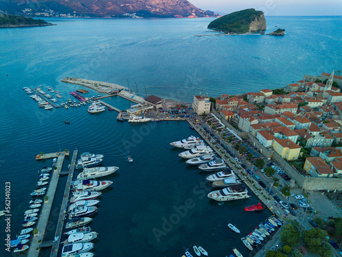 Port with ships and boats for excursions on the Adriatic Sea near the island of St. Stevan in the evening city of Budva against a romantic cloudy sky