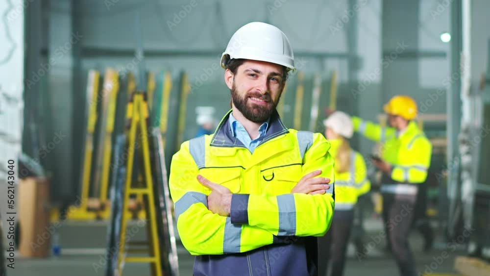 Portrait shot of handsome young Caucasian male in helmet and yellow uniform standing at plant and smiling to camera. Indoors. Man worker at manufactory. Producing concept. Manufactory place. Portrait shot of handsome young Caucasian male in helmet and yellow uniform standing at plant and smiling to camera. Indoors. Man worker at manufactory. Producing concept. Manufactory place.