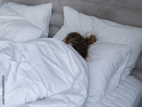 Young woman sleeping in white sheets in a bed, at home or in a hotel room.