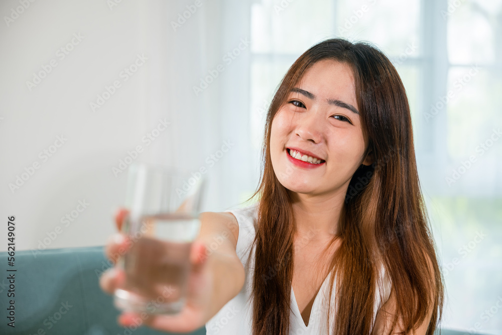 Happy smiling female beauty with water glass for drink in living room, Portrait of Asian young woman holding drinking nature water on hand at home, Healthy lifestyle Happy smiling female beauty with water glass for drink in living room, Portrait of Asian young woman holding drinking nature water on hand at home, Healthy lifestyle
