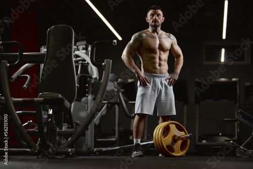 Portrait of young muscular man posing shirtless in gym indoors with barbell equipment. Relief body shape. Concept of sport, workout, strength