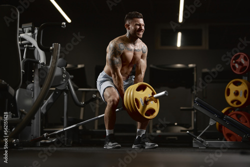 Power. Portrait of young muscular man training shirtless in gym indoors. Lifting barbell exercise. Relief body shape. Concept of sport  workout  strength