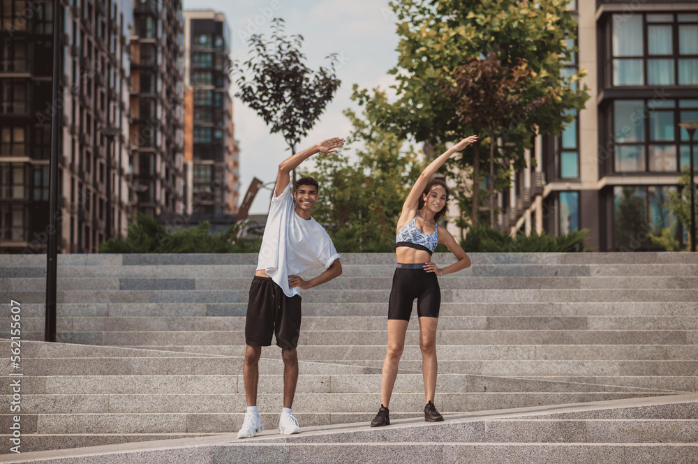Cheerful couple performing a stretching exercise on the steps Cheerful couple performing a stretching exercise on the steps