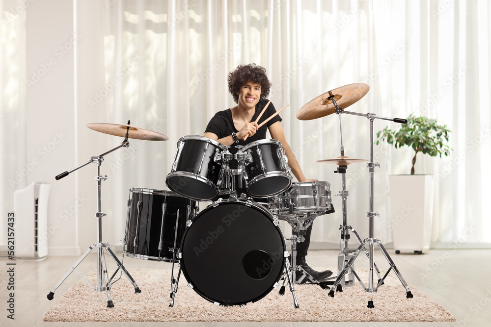Fototapeta premium Young male drummer holding drumsticks and smiling in a room