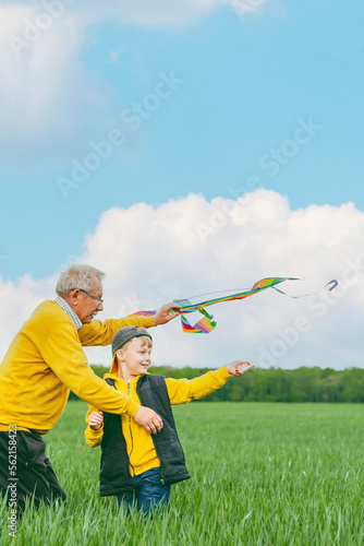 A happy senior man with his grandson preparing for launch a kite on a green glade. family active outdoor games. Healthy life concept. 