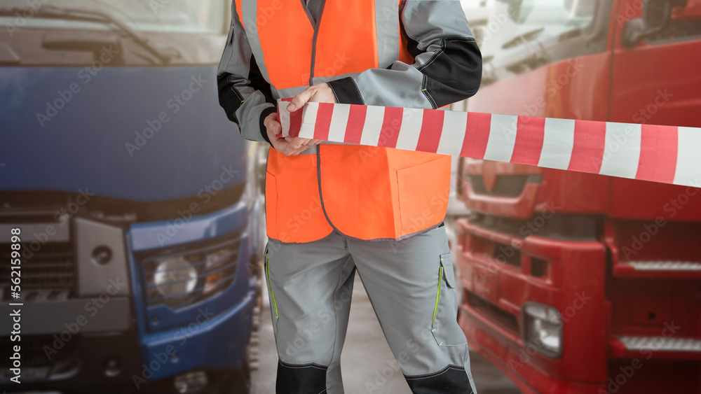 Naklejka premium Man in special clothes blocks the parking with a tape. Different semi trucks on the background