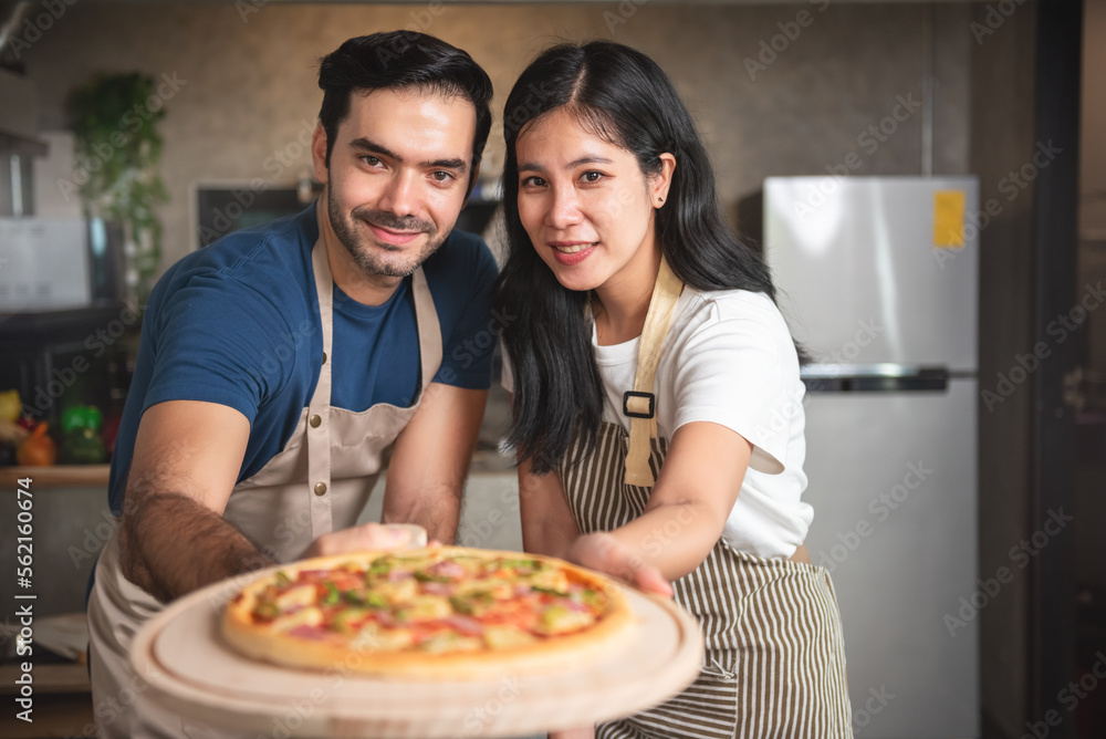 Young couple family caucasian man and asian women wearing aprons enjoy making pizza at home kitchen. Small business restaurant and cuisine. Young couple family caucasian man and asian women wearing aprons enjoy making pizza at home kitchen. Small business restaurant and cuisine.