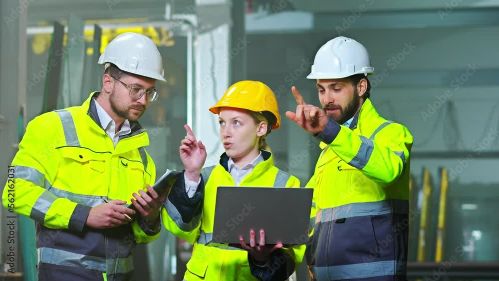 Caucasian men and woman colleagues at manufactory talking and discussing work with laptop computer. Production plant. Indoors. Males and female co-workers at factory. Construction site. Builders. Caucasian men and woman colleagues at manufactory talking and discussing work with laptop computer. Production plant. Indoors. Males and female co-workers at factory. Construction site. Builders.