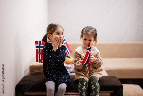 Canvas Print Two sisters are sitting on a couch at home with norwegian flags on hands