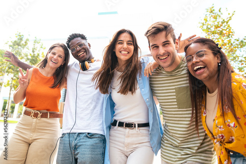 Low angle view of a happy group of multiracial friends looking at camera, enjoying outdoors. Multiethnic cheerful young people