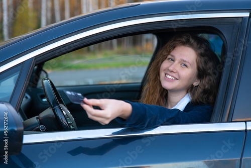 Beautiful happy cheerful girl, young positive woman is paying with credit plastic card from her car smiling, holding out bank card from opened automobile window. Payment for purchases, fast food auto