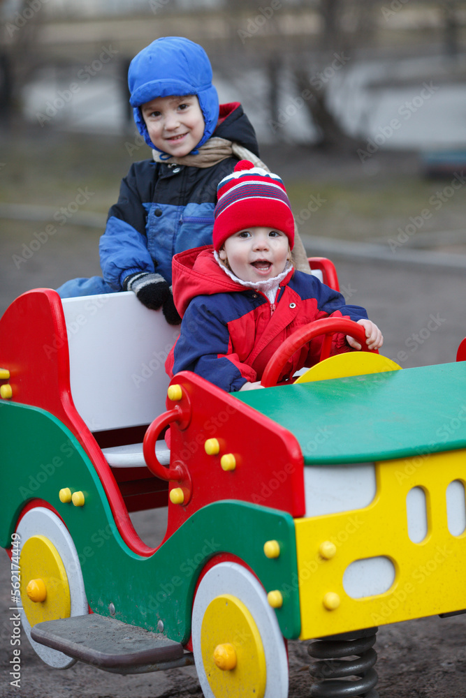 Two small children play with a car on the playground during the cold season.