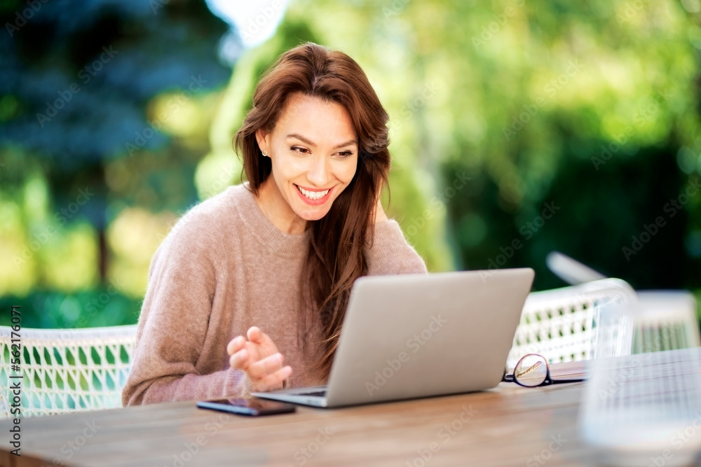 Excited middle aged woman using a laptop while sitting on balcony at home Excited middle aged woman using a laptop while sitting on balcony at home