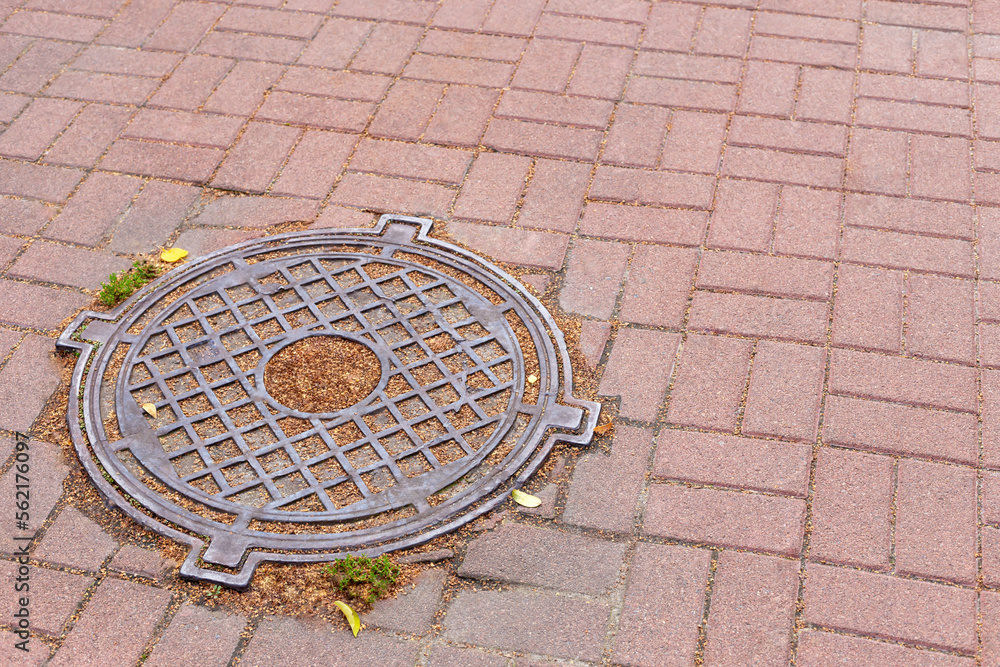 Iron sewer manhole on the ground among the tiles