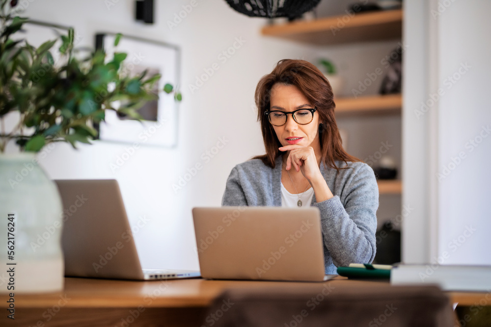 Attractive middle aged business woman sitting at home and using laptop for work Attractive middle aged business woman sitting at home and using laptop for work