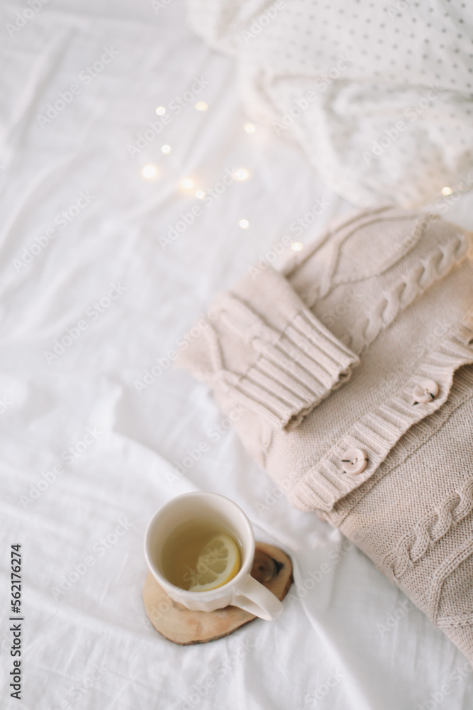 Knitted beige sweater and cup of tea on messy bed background. Winter and spring fashion concept. Top view flat lay. Knitted beige sweater and cup of tea on messy bed background. Winter and spring fashion concept. Top view flat lay.