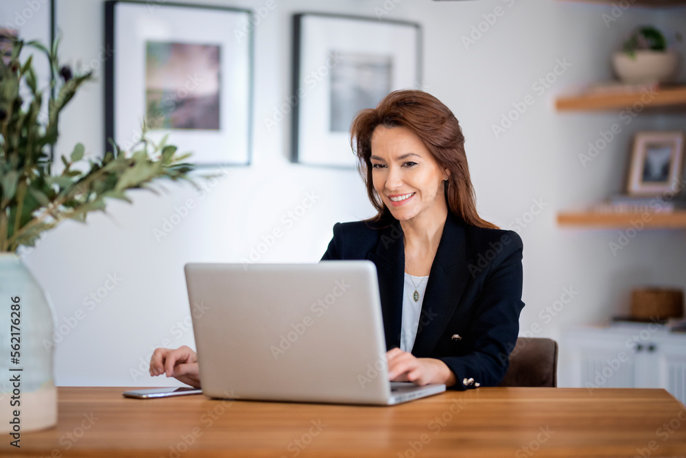 Attractive middle aged businesswoman sitting at home and using laptop for work Attractive middle aged businesswoman sitting at home and using laptop for work