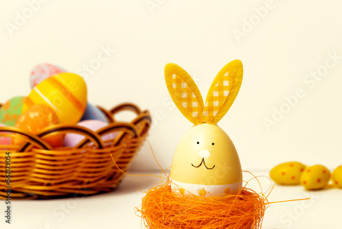 Easter egg with rabbit ears in a wicker nest on the background of a basket with painted eggs. Easter card.