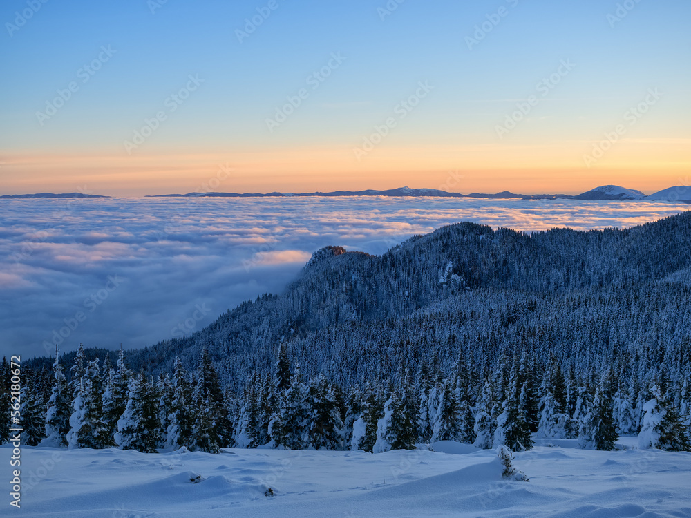 Aerial view of distant mountain peaks above clouds in clear sunny blue sky at sunrise.