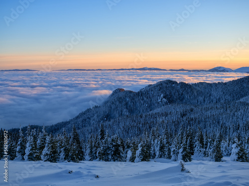 Aerial view of distant mountain peaks above clouds in clear sunny blue sky at sunrise. © Daniel CHETRONI