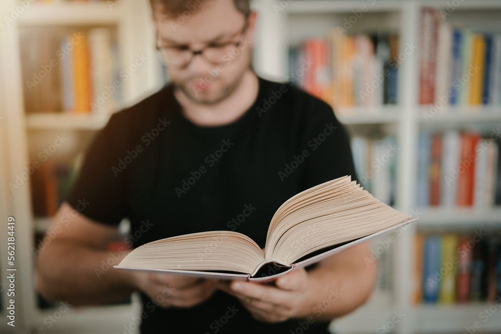 Man holding an open book. Man is reading book. Blurred books in background. Man holding an open book. Man is reading book. Blurred books in background.