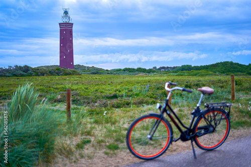 Dutch lighthouse on green heath. ladies bike out of focus on the road. Landscape at dawn. Netherlands, Zuid-Holland, Goeree-Overflakkee, Ouddorp.