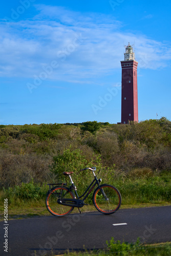 Dutch lighthouse on a hill. Bicycle on wet road. Landscape shot in the morning. Blue sky for copy space. Netherlands, Zuid-Holland, Goeree-Overflakkee, Ouddorp.
