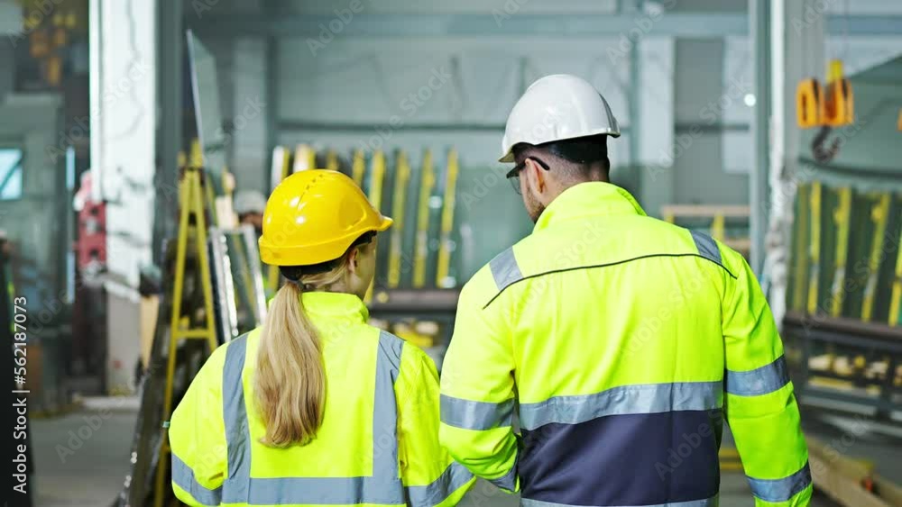 Rear of Caucasian man and woman colleagues at manufactory walking and talk while discussing work or planning. Production. Inside. Back view of male and female co-workers stepping at producing site. Rear of Caucasian man and woman colleagues at manufactory walking and talk while discussing work or planning. Production. Inside. Back view of male and female co-workers stepping at producing site.