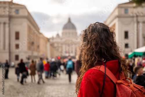 Woman in red coat looking at St. Peter's Basilica in Rome from the bridge that leads straight up to it