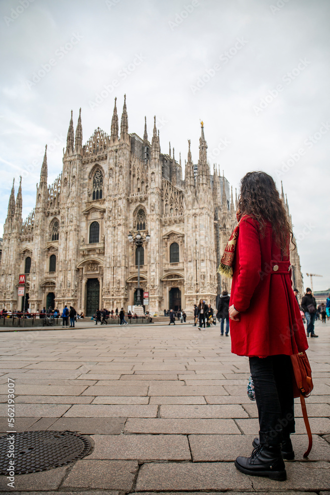 Woman in red coat looking at the Duomo in Milan in Italy, in cloudy day