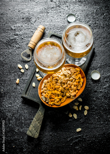 Two glasses of beer and peanuts in a bowl on a black cutting Board.