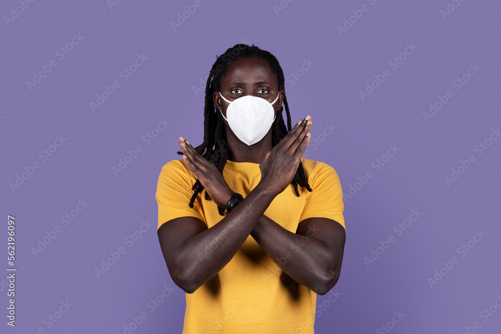 Black guy in protective medical mask gesturing stop on purple Black guy in protective medical mask gesturing stop on purple
