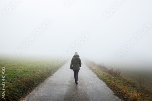 Lonely woman walks on empty road in fog. Journey to unknown place © encierro