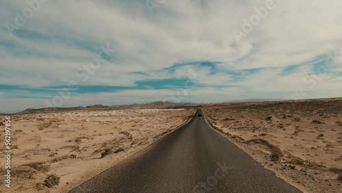 Motion on an empty road going into the distance to arid desert rocks in desertic landscape in the dried sand desert. The highway with black asphalt without markings. Beautiful cloudy sky in background