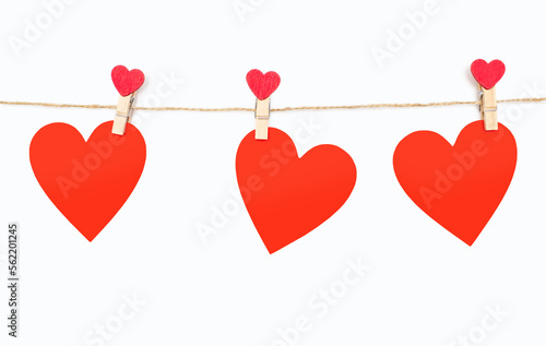 Three red hearts are attached to a rope with clothespins on a white background. Beautiful decor in the form of hearts or decoration for Valentine's Day. Three red hearts made of wood