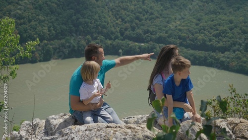 Parents with children sitting on top cliff and admire mountain river landscape