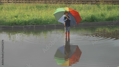 Little child standing in a puddle with colored umbrella