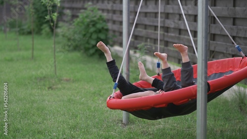 Two kids playing barefoot in the yard spinning nest swing