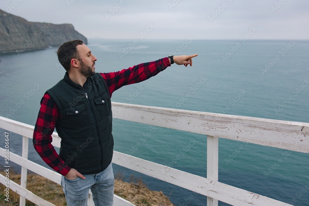 
Side view of a tourist pointing with his hand in the right direction.
Man traveler explores the area. Healthy lifestyle and outdoor activities near the sea.