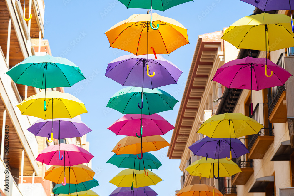 Street with bright, multi-colored umbrellas against the sky with houses.