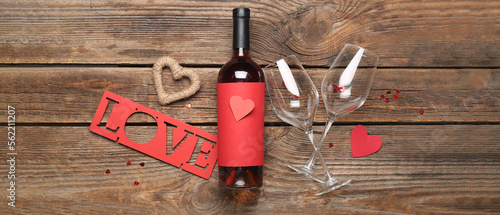 Bottle of wine, glasses, hearts and word LOVE on wooden background. Valentine's Day celebration